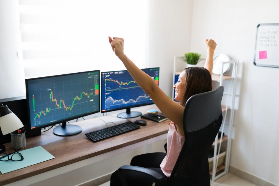 Person looking at graphs and charts raising their arms in celebration because the stock market went up.