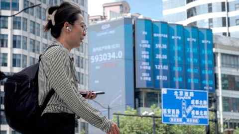 A woman walking past a screen showing stock exchange data in Shanghai, China